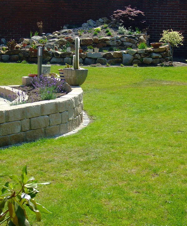 Neu gestalteter Garten mit Sandsteinmauer und Rasenfläche von Lansmann